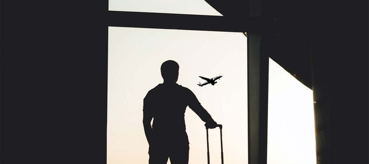 man standing with suitcase in an airport looking at airplane